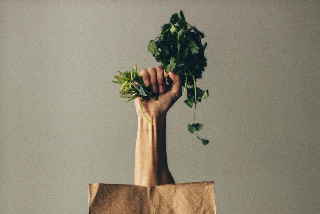 Hand kommt aus brauner Papier-Einkaufstüte, hält ein Bund Petersilie