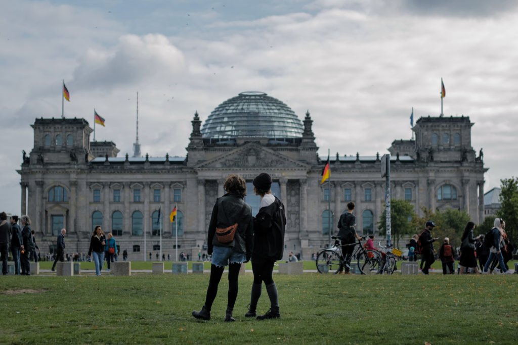 Menschen auf Bänken auf einer Wiese, Zelte im Hintergrund