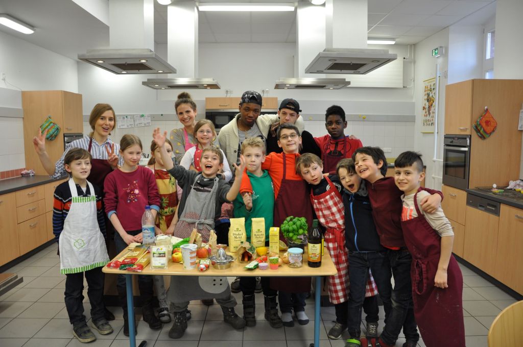 Gruppe von Kindern, Jugendlichen und Erwachsenen vor einem Tisch mit Lebensmitteln