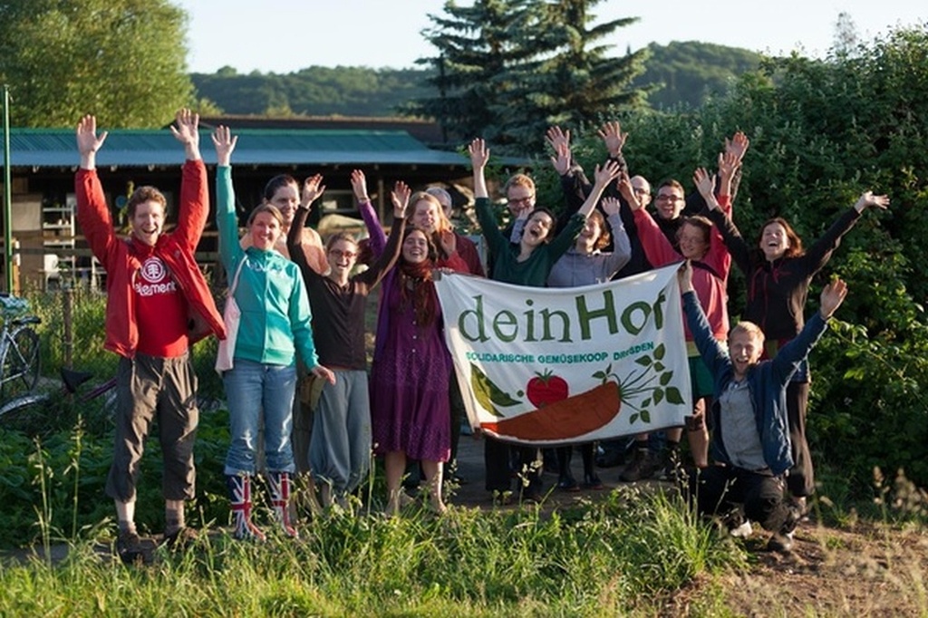 Gruppe fröhlicher Menschen, die ein Banner mit dem Schriftzug Dein Hof hochhalten