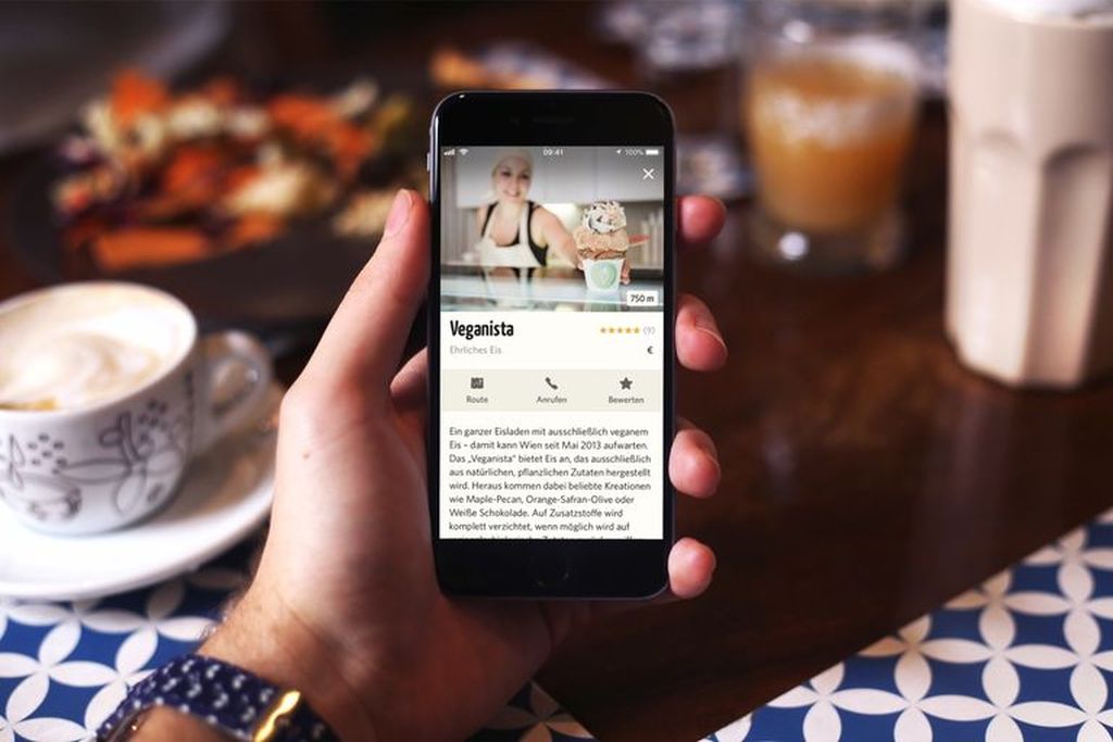 Eine Hand hält ein Smartphone auf dessen Display das Profil eines Restaurants abgebildet ist. Abgegebene Bewertungen sind zu erkennen. Die Funktionen "Route", "Anrufen" und "Bewerten" können ausgewählt werden.