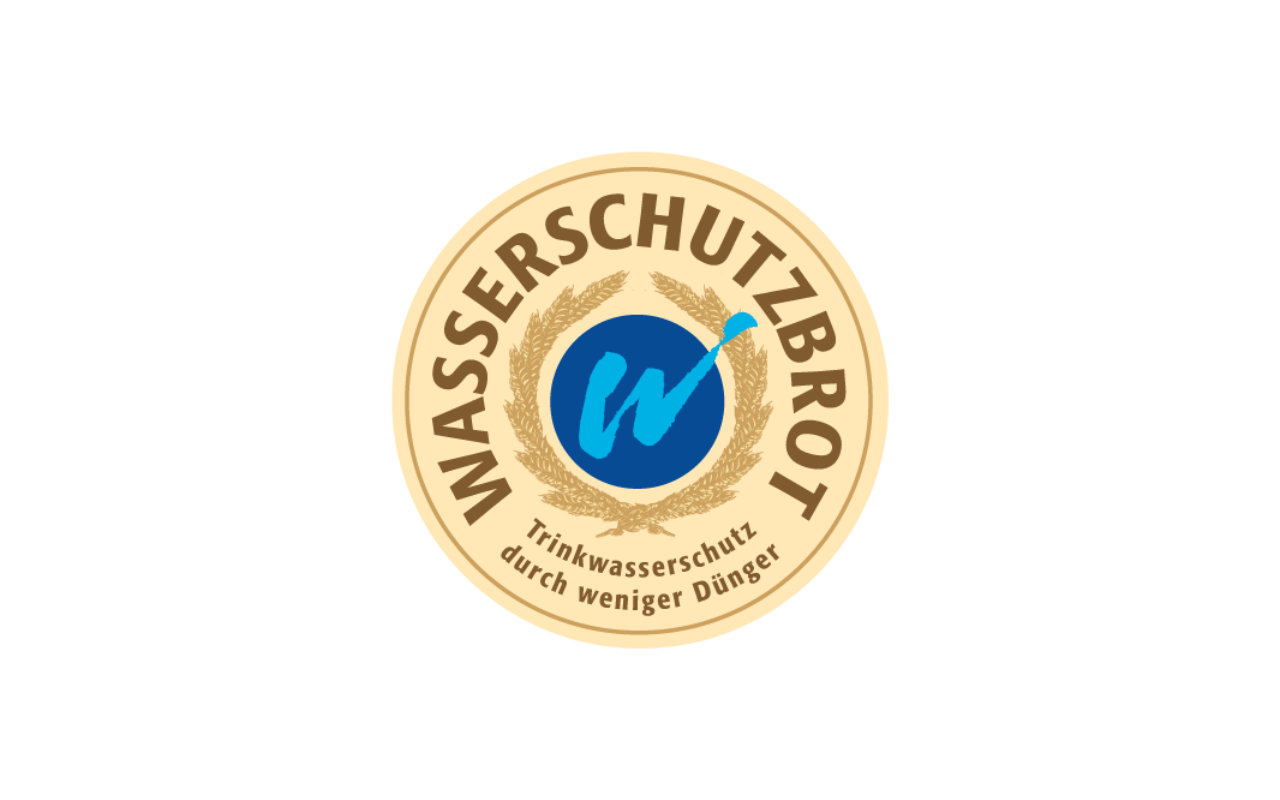 Logo Wasserschutzbrot, Blaues W auf blauem Grund, eingefasst in hellbraunen Kreis mit Schriftzug